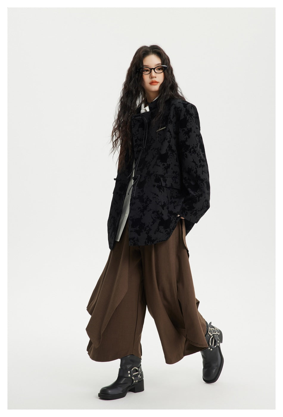Three-quarter view of a model wearing a black abstract-patterned toggle-front jacket over a white shirt and brown wide-leg