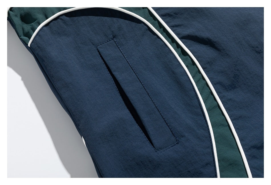 Close-up of a vertical pocket opening on a navy jacket, alongside white piping and a dark green panel.