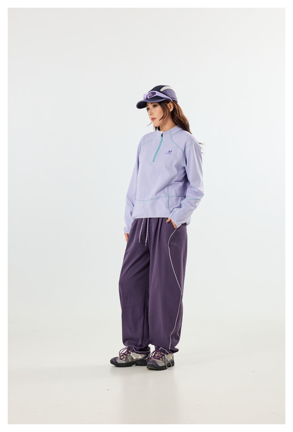 A model wears a lavender quarter-zip pullover with pale contrast seams and loose purple pants.