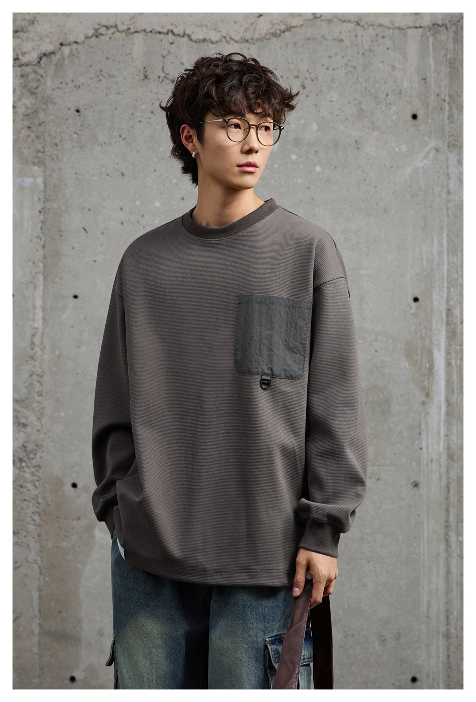 Model wearing a charcoal gray oversized sweatshirt with a dark chest pocket and blue jeans.