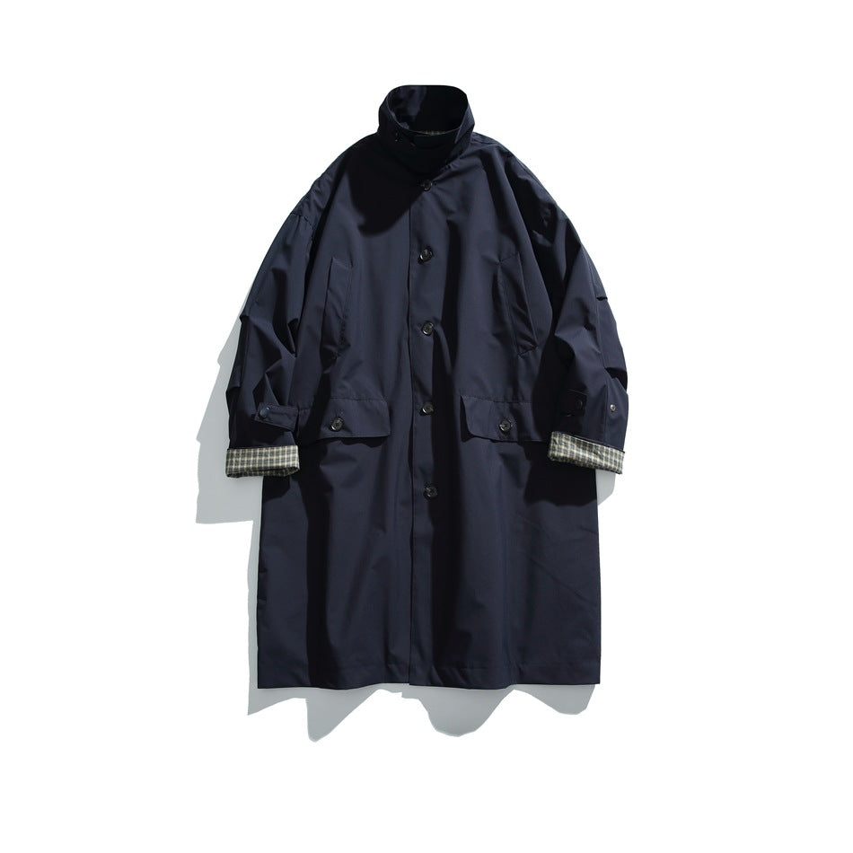 Navy long button-front coat with stand collar, flap pockets and plaid cuff lining, flat lay front view