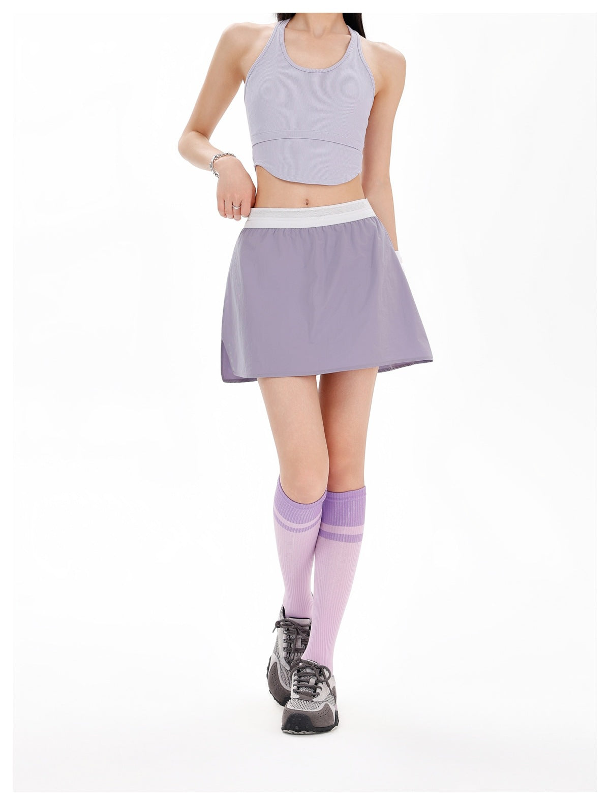 Front view of a model wearing a lilac racerback crop top and matching flared mini skirt with a white waistband.