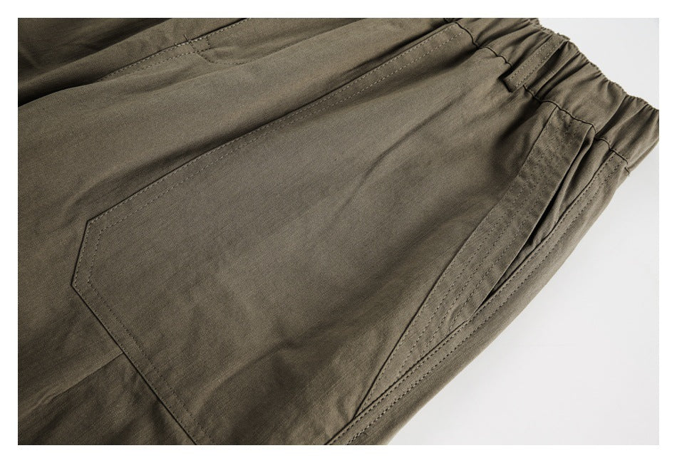 Close-up of olive-brown trousers showing an angled pocket seam and gathered elastic waistband.