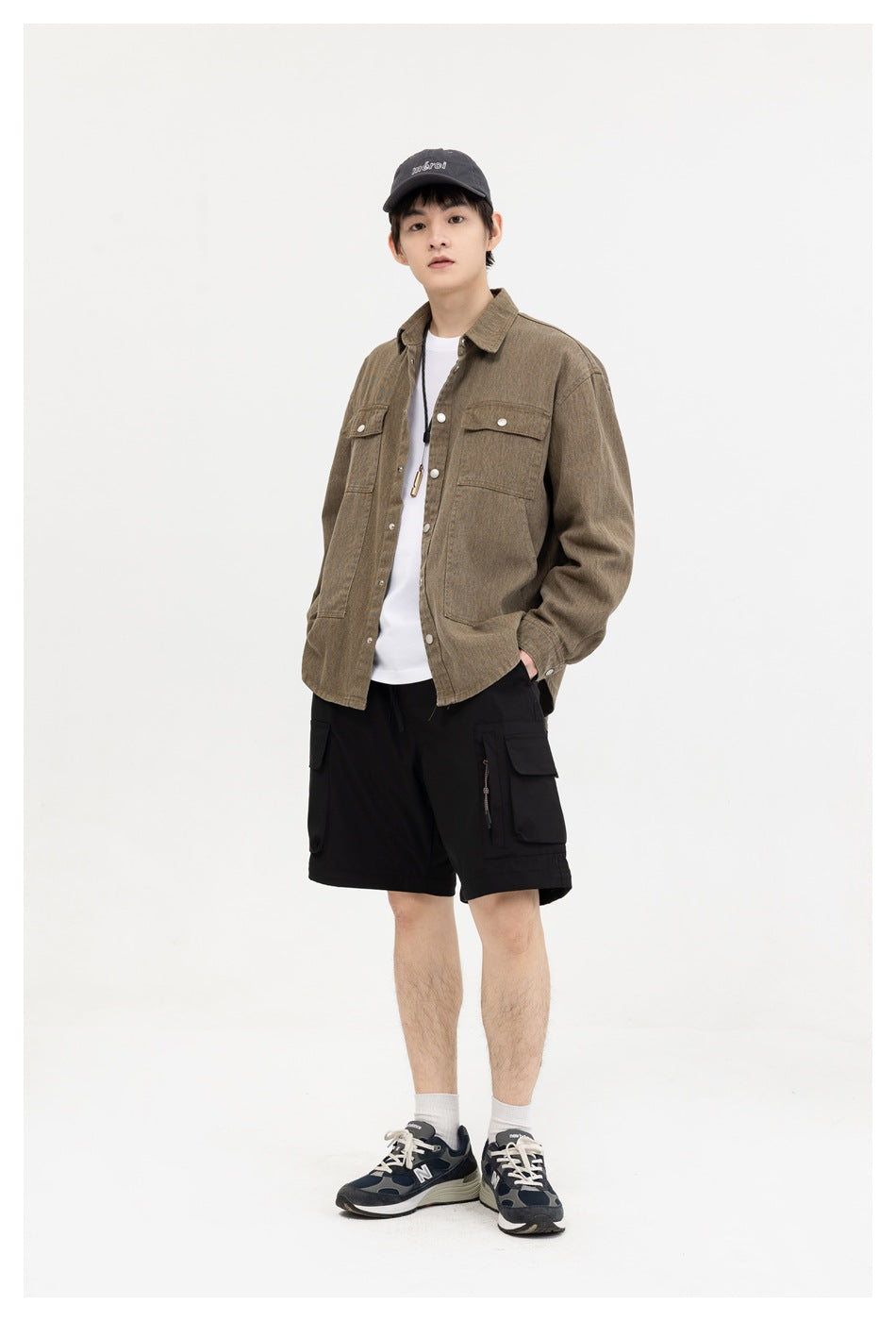 A model wears a brown pocketed overshirt open over a white shirt, with black cargo shorts, in a three-quarter view.