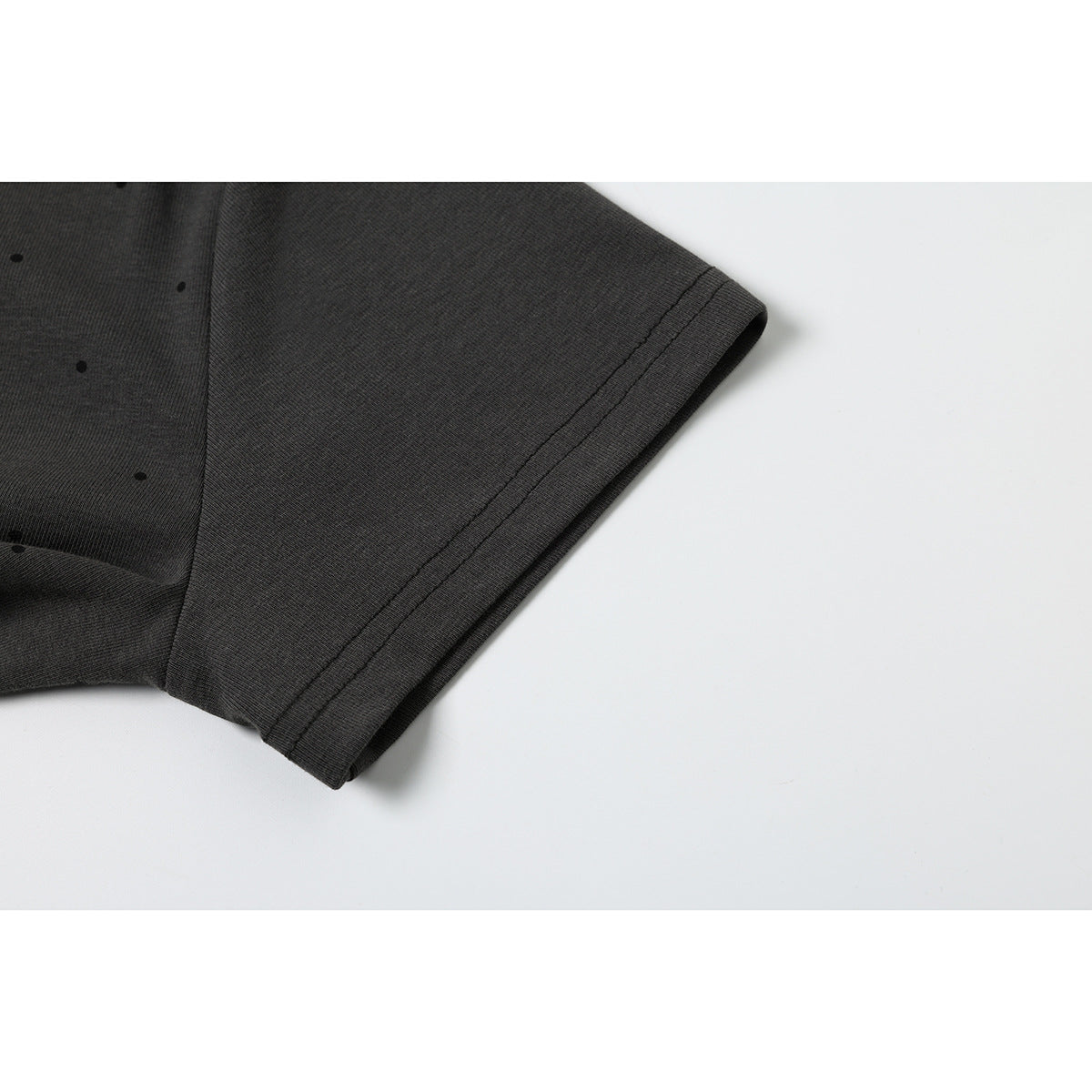 Close-up of the charcoal T-shirt's short sleeve and double-stitched hem, with a few small black dots.