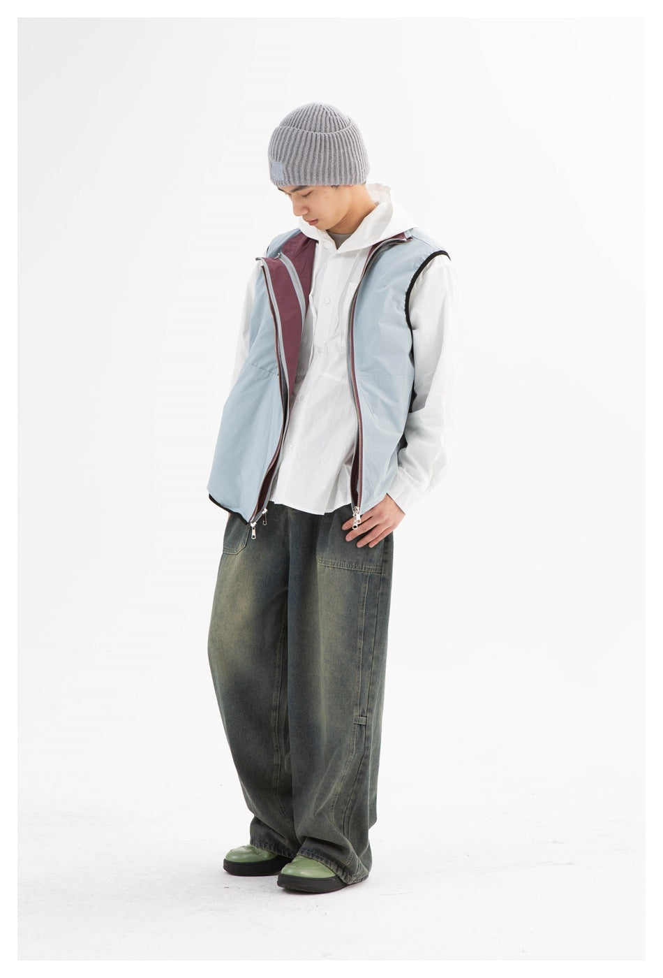 Model wearing a pale blue sleeveless zip vest with burgundy lining, a white shirt, dark wide-leg jeans and a gray beanie.
