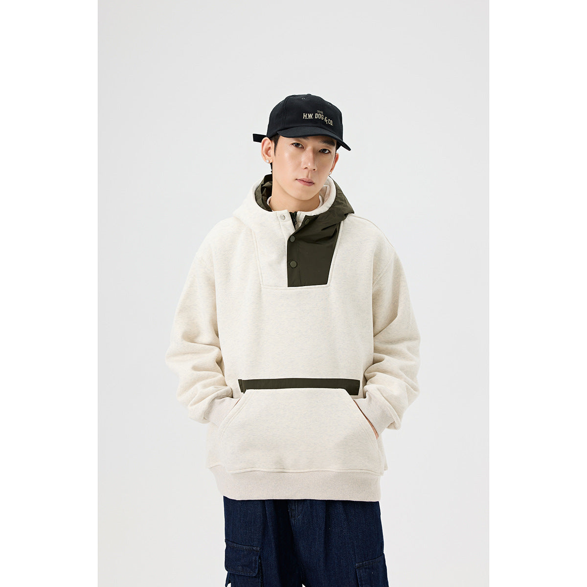 Model wearing an ivory pullover hoodie with an olive hood panel, snap placket and kangaroo pocket.