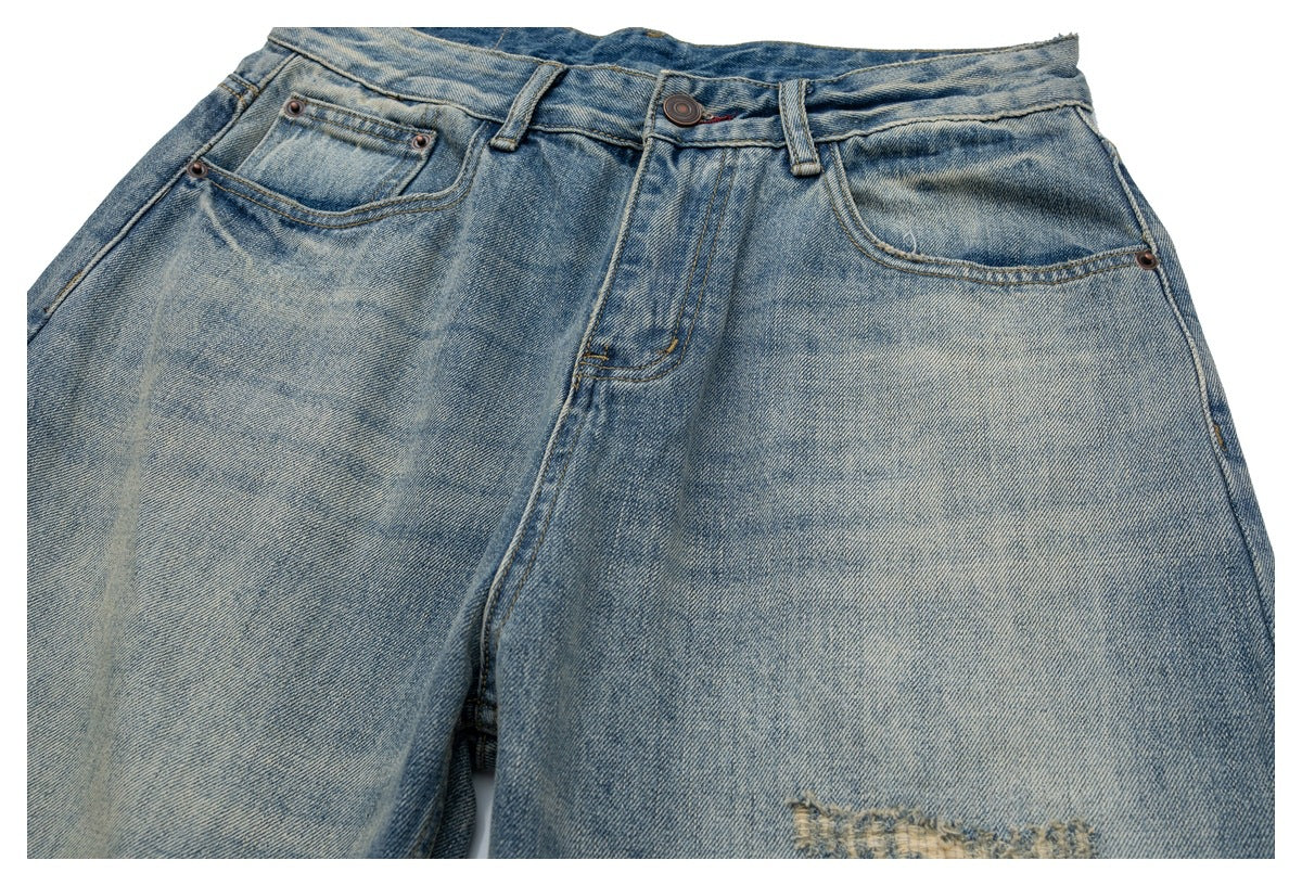Close-up of the front of faded blue jeans showing the waistband, button, pockets and distressed detailing near the thigh.