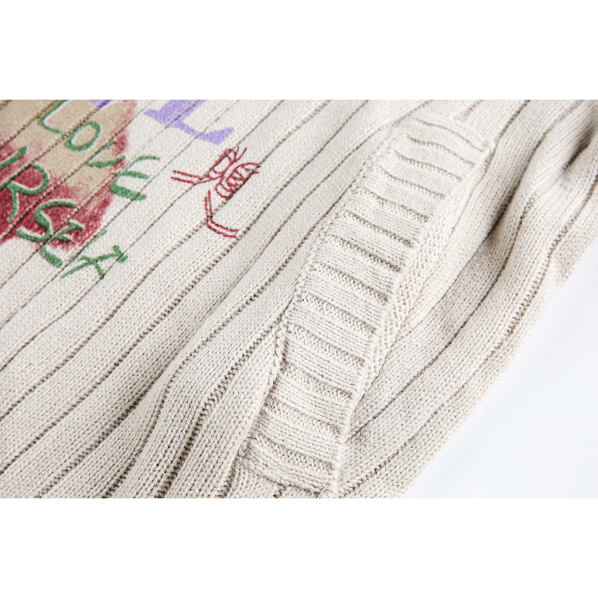 Close-up of the ivory sweater's ribbed knit seams and sleeve edge beside part of its colorful graphic.
