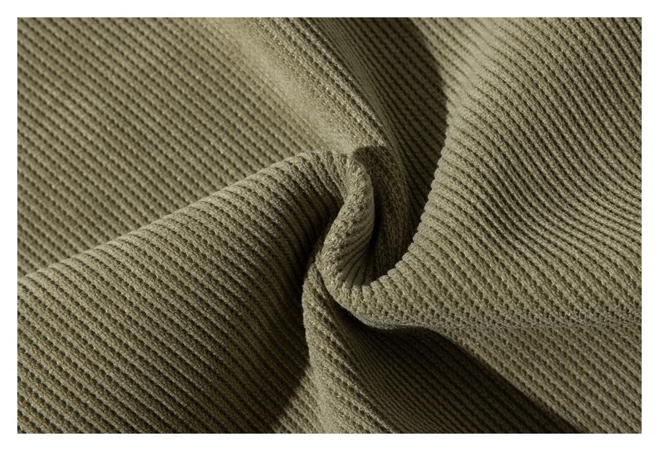 Close-up of olive ribbed garment fabric folded to show its textured surface.