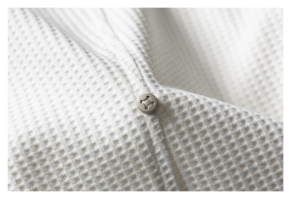 Close-up of a single button fastening on ivory waffle-knit fabric.
