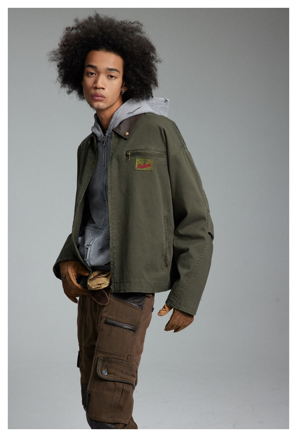 Three-quarter view of a model wearing an olive jacket with a brown collar and gray hoodie.