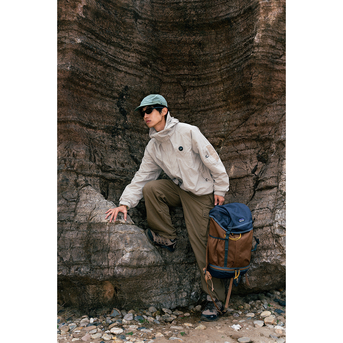 A person models a light gray hooded outdoor jacket with olive trousers against a rocky backdrop.