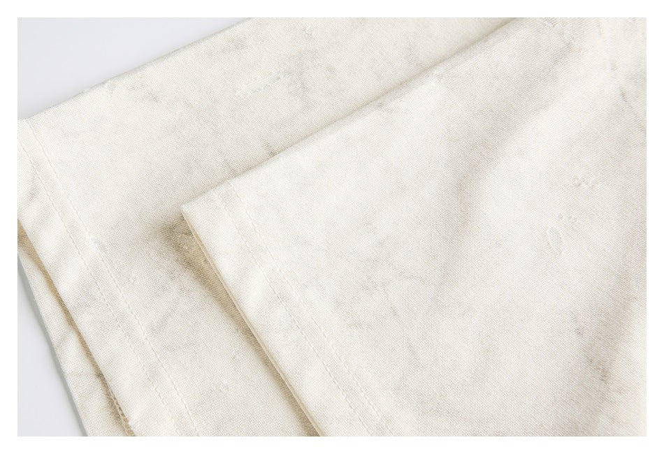 Close-up of overlapping ivory garment panels with seams and scattered distressed marks.