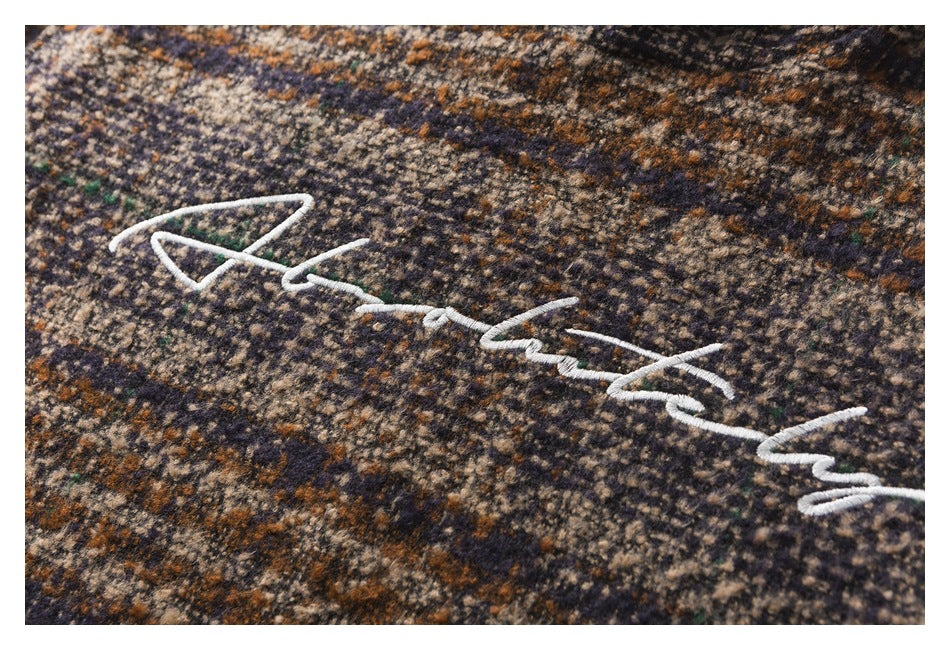 Close-up of white cursive embroidery on mottled brown, navy, beige, and green patterned fabric.