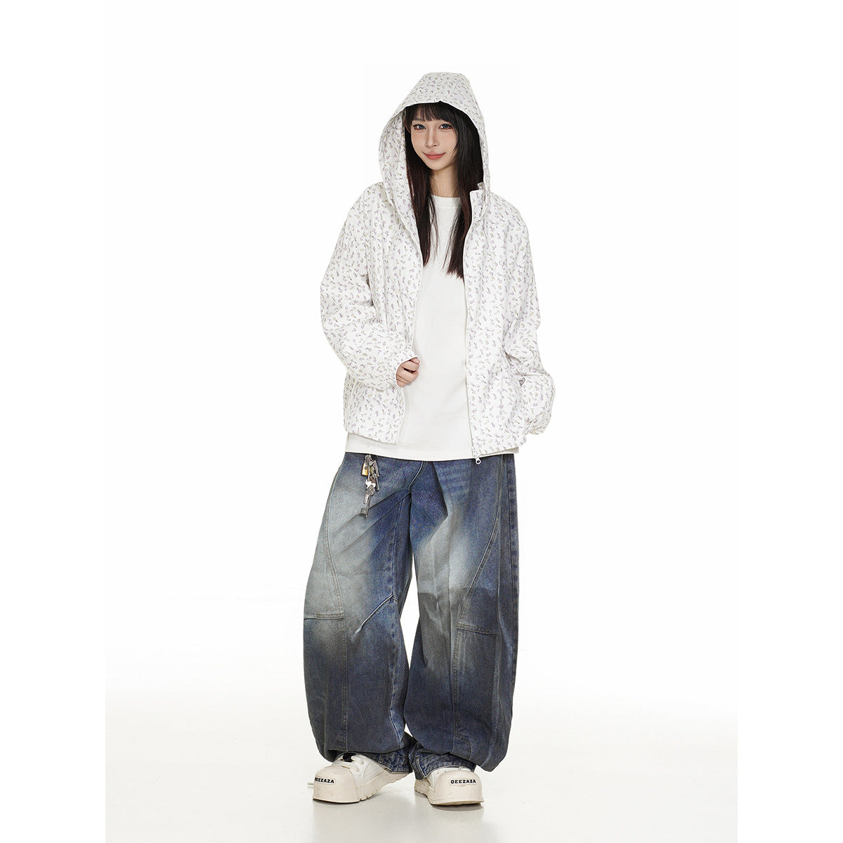 Model wearing a white zip-up hooded jacket with a tiny floral print, hood up, and loose dark blue jeans.