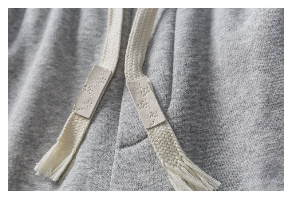 Close-up of cream braided drawstrings with stitched end tabs against heather-gray fabric.