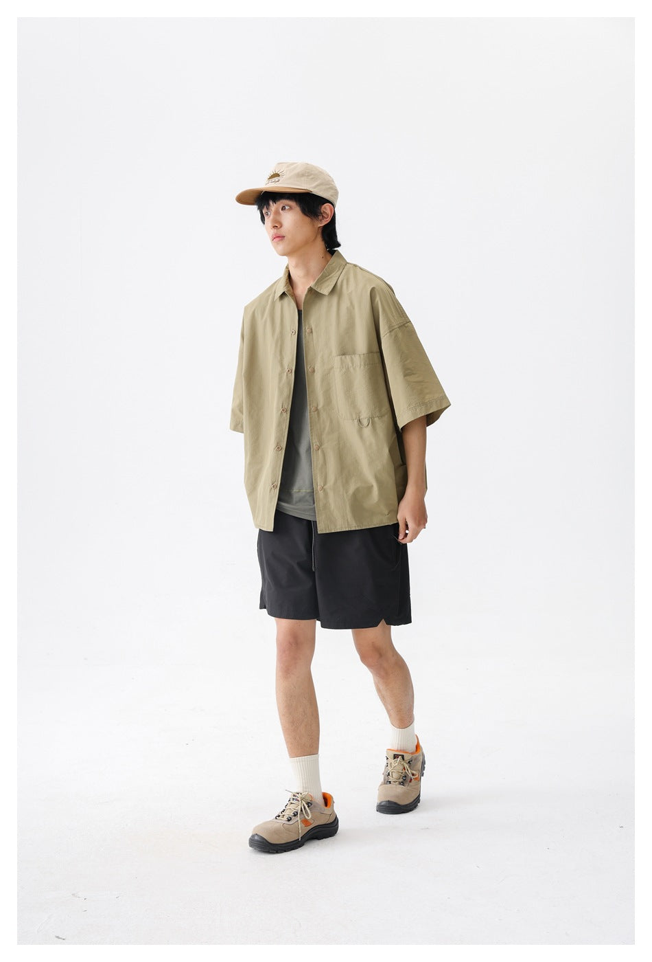 Three-quarter view of a model wearing an olive-khaki short-sleeve button-up shirt and black shorts.