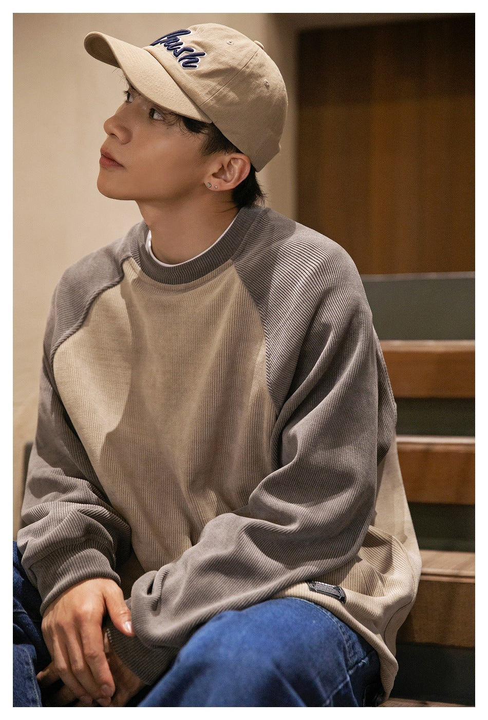 Close view of a man wearing a taupe sweatshirt with gray raglan sleeves and a beige embroidered cap.