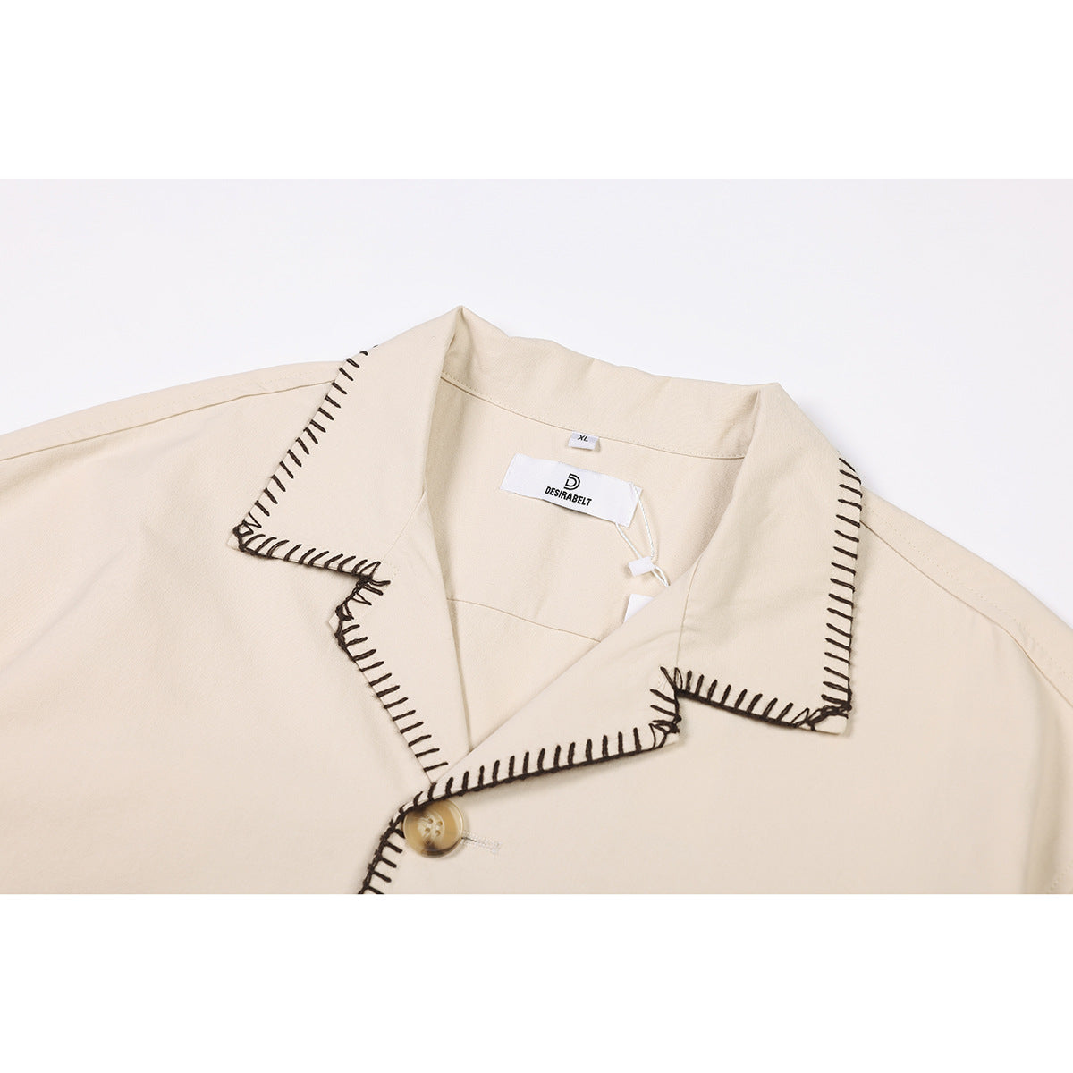 Close-up of a cream shirt's notched collar with dark blanket stitching, a button, and an inside neck label.