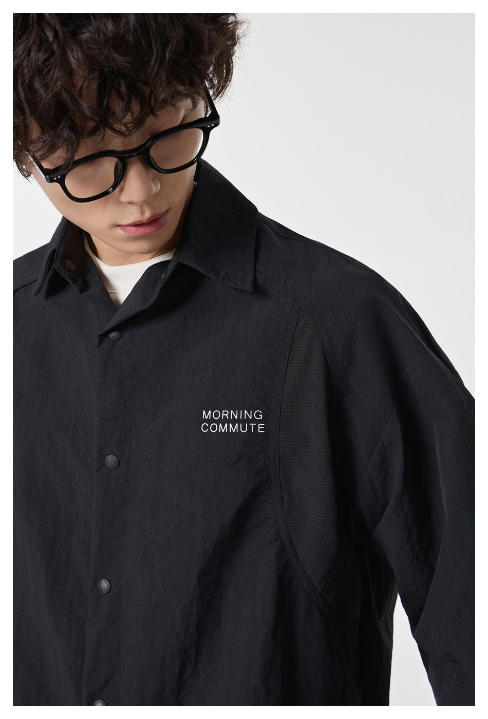 Close-up of the black overshirt's collar, snap buttons, curved side panel, and white chest lettering.