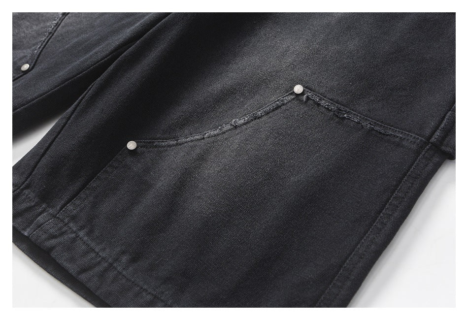 Close-up of black textured trousers showing a curved pocket opening with two silver rivets and reinforced stitching.