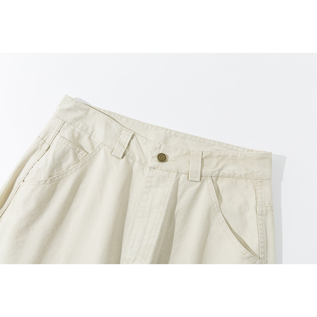 Close-up of cream trousers showing the waistband, button, belt loops, and curved front pockets.