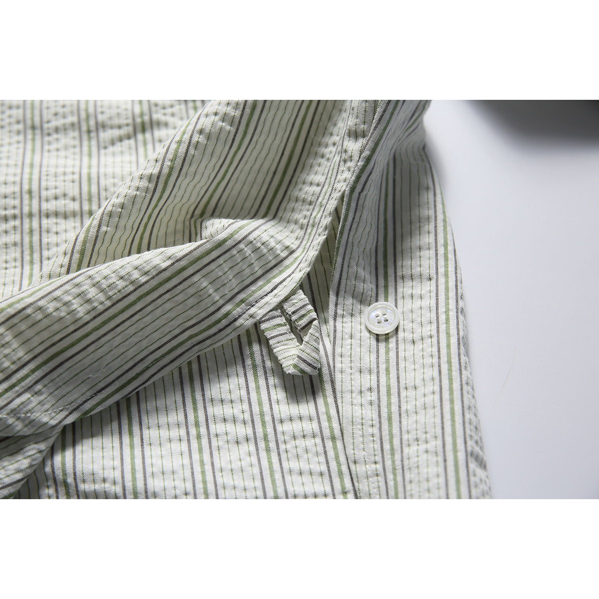 Close-up of a white button and cuff area on an off-white shirt with narrow gray and muted green stripes.