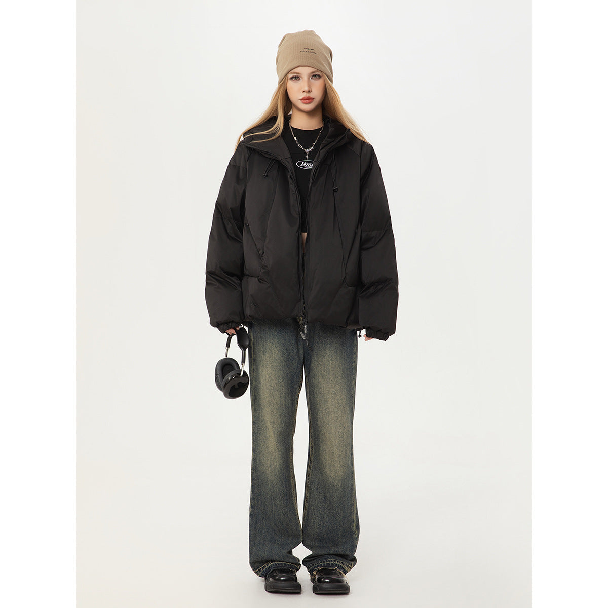 Front full-body view of a model wearing a black puffer jacket, beige beanie and loose dark jeans.
