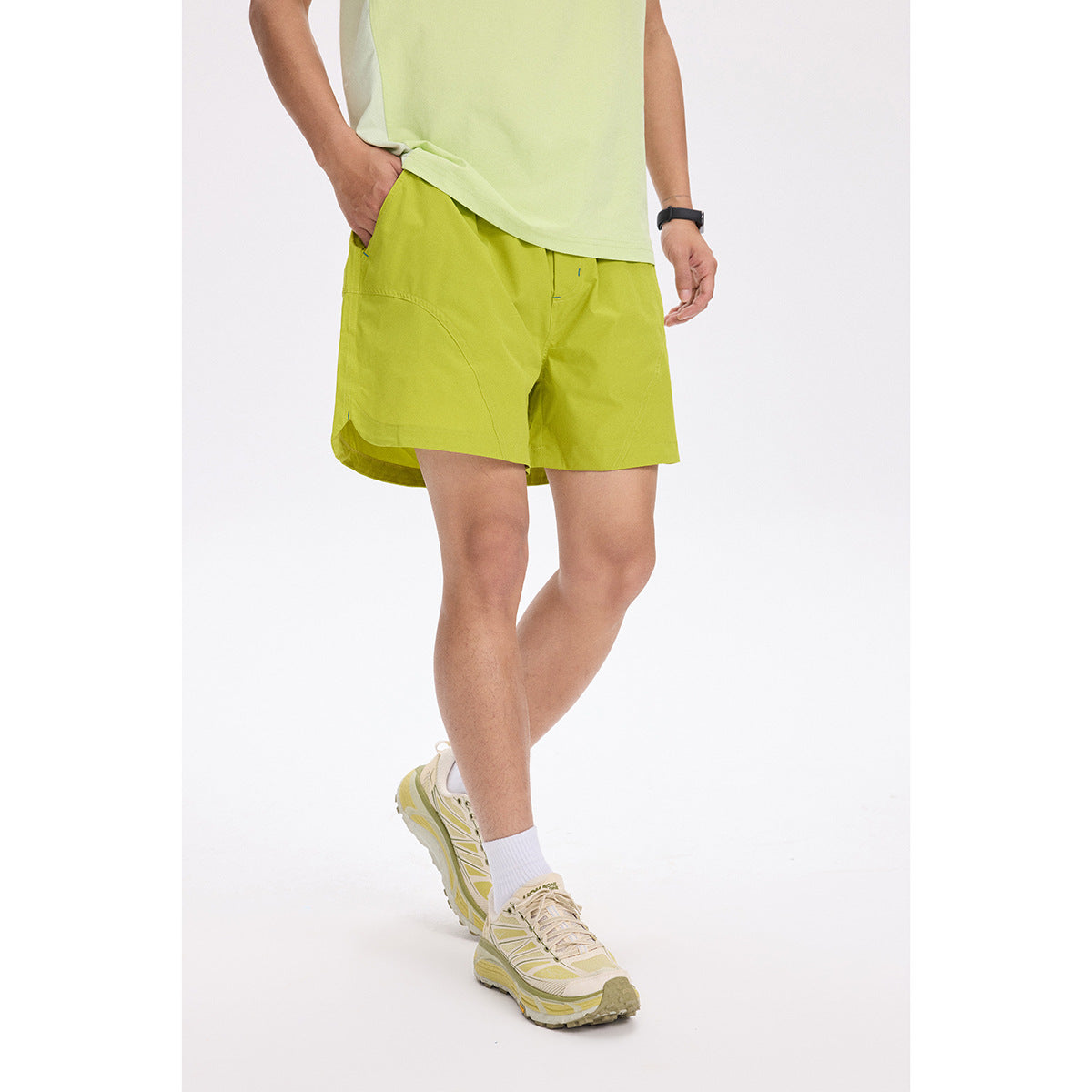 Cropped model wearing bright lime-green shorts with curved pockets and a pale green top, shown from the front.