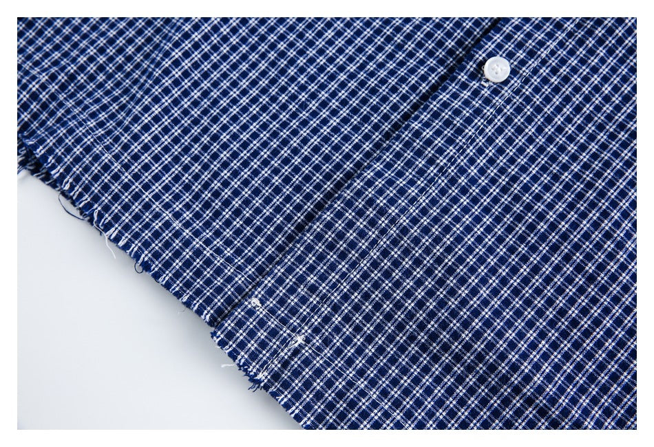 Close-up of navy and white plaid garment fabric with a white button and a frayed edge.
