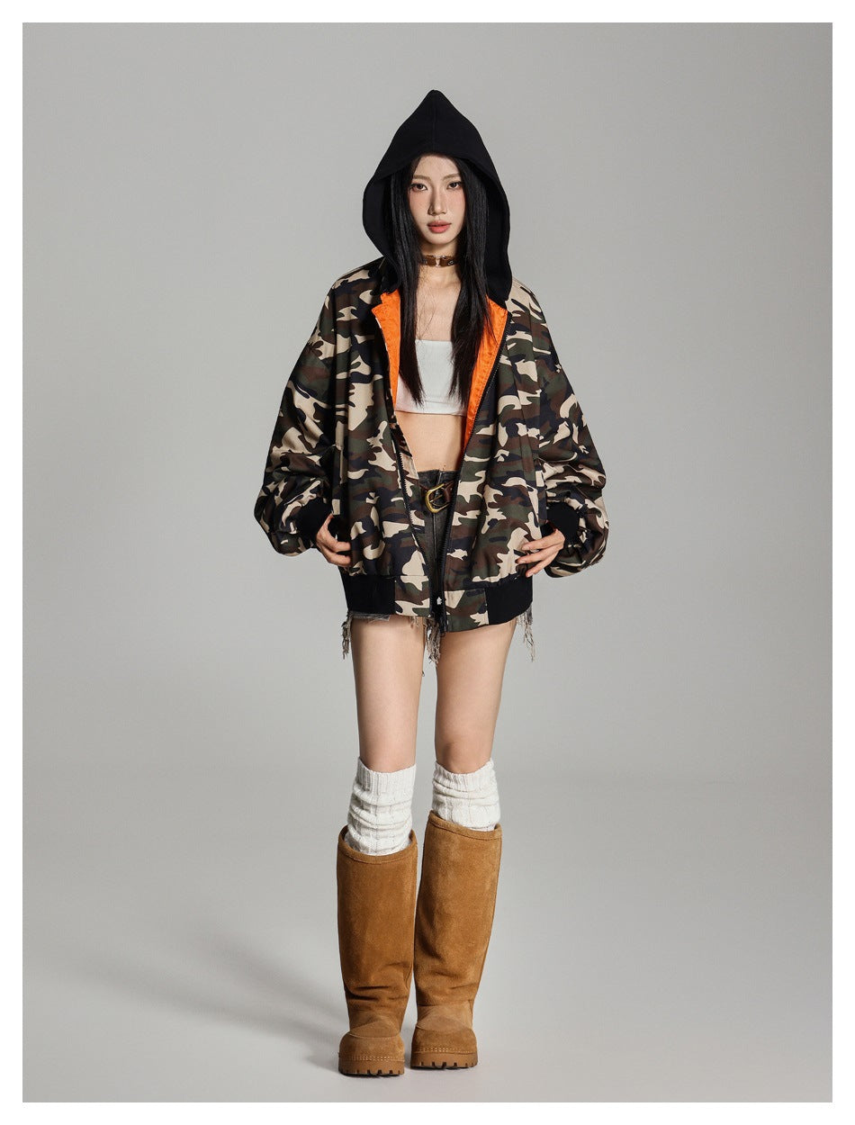 Full-length front view of a model in an open camouflage hooded jacket with bright orange lining and black trim.