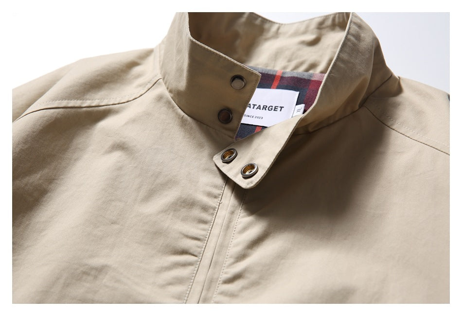 Close-up of a beige jacket's stand collar, snap closures and front placket; plaid lining and an inner label show.