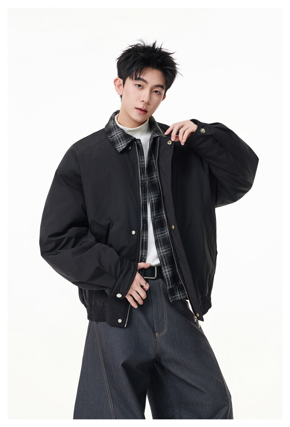 Model wearing an open black jacket with a plaid collar over a plaid shirt and white top.