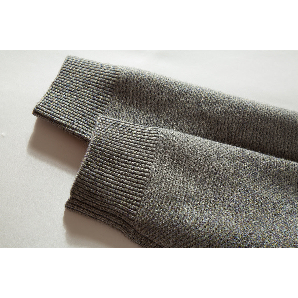 Close-up of two gray cardigan sleeves with wide ribbed cuffs and textured knit fabric.