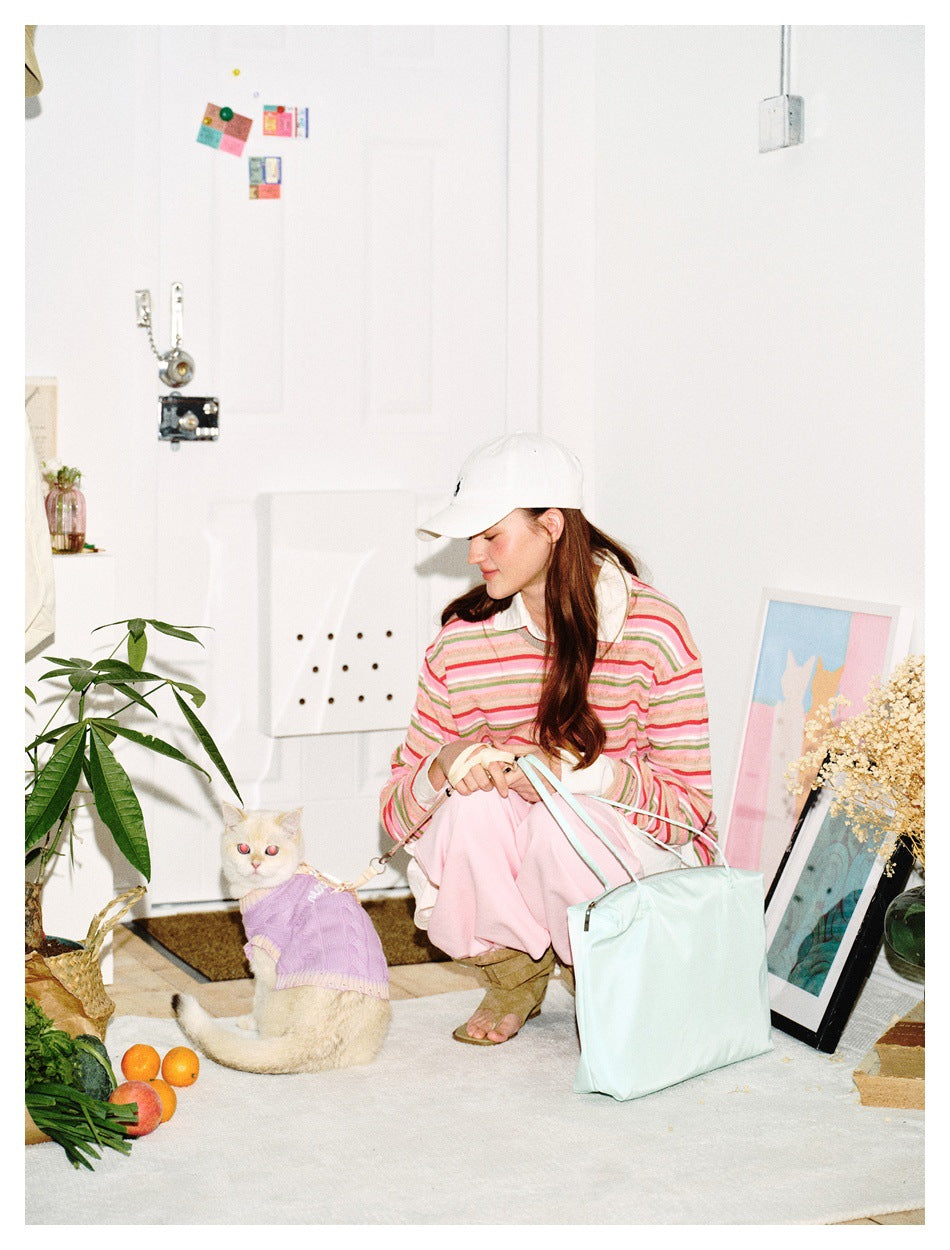 Model seated beside a cat, wearing a pink, green and white striped long-sleeve top and pink trousers.