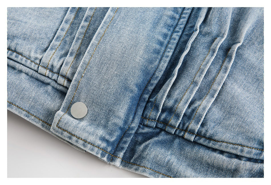 Close-up of a silver snap and stitched edge on a light blue denim jacket.