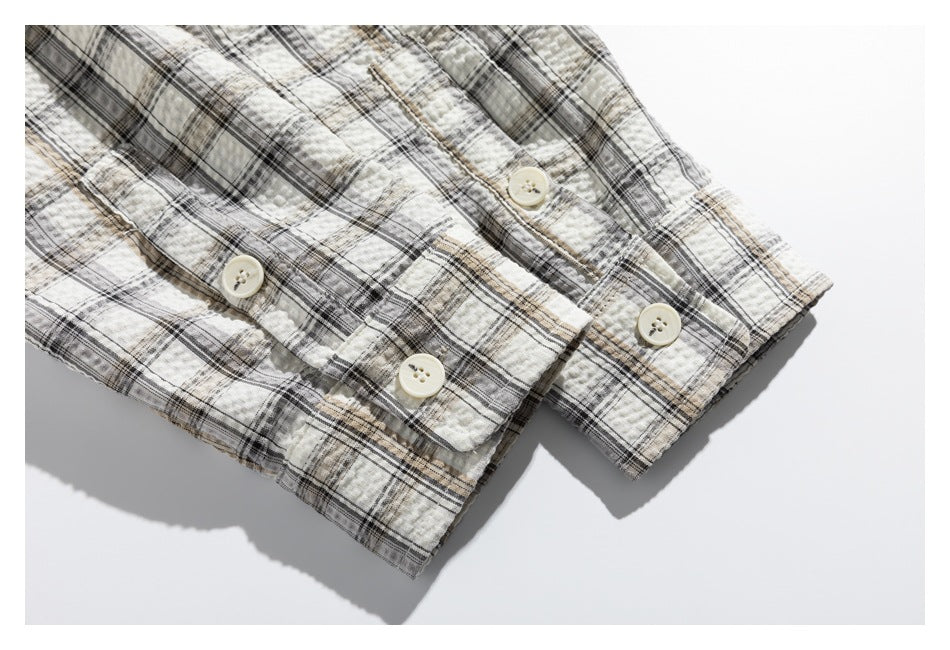 Close-up of a cream, black, and tan plaid shirt cuff with several cream buttons.