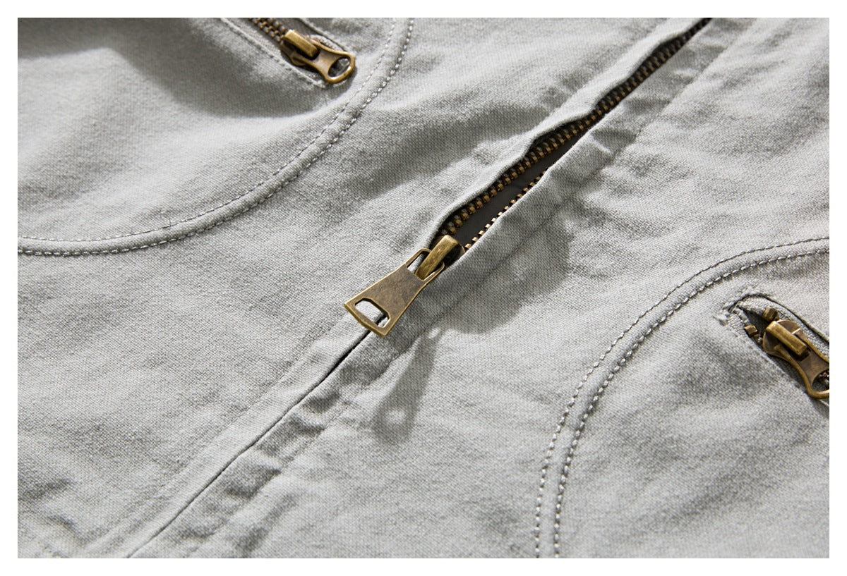 Close-up of the light gray jacket's brass front zipper and curved stitched pocket edges.