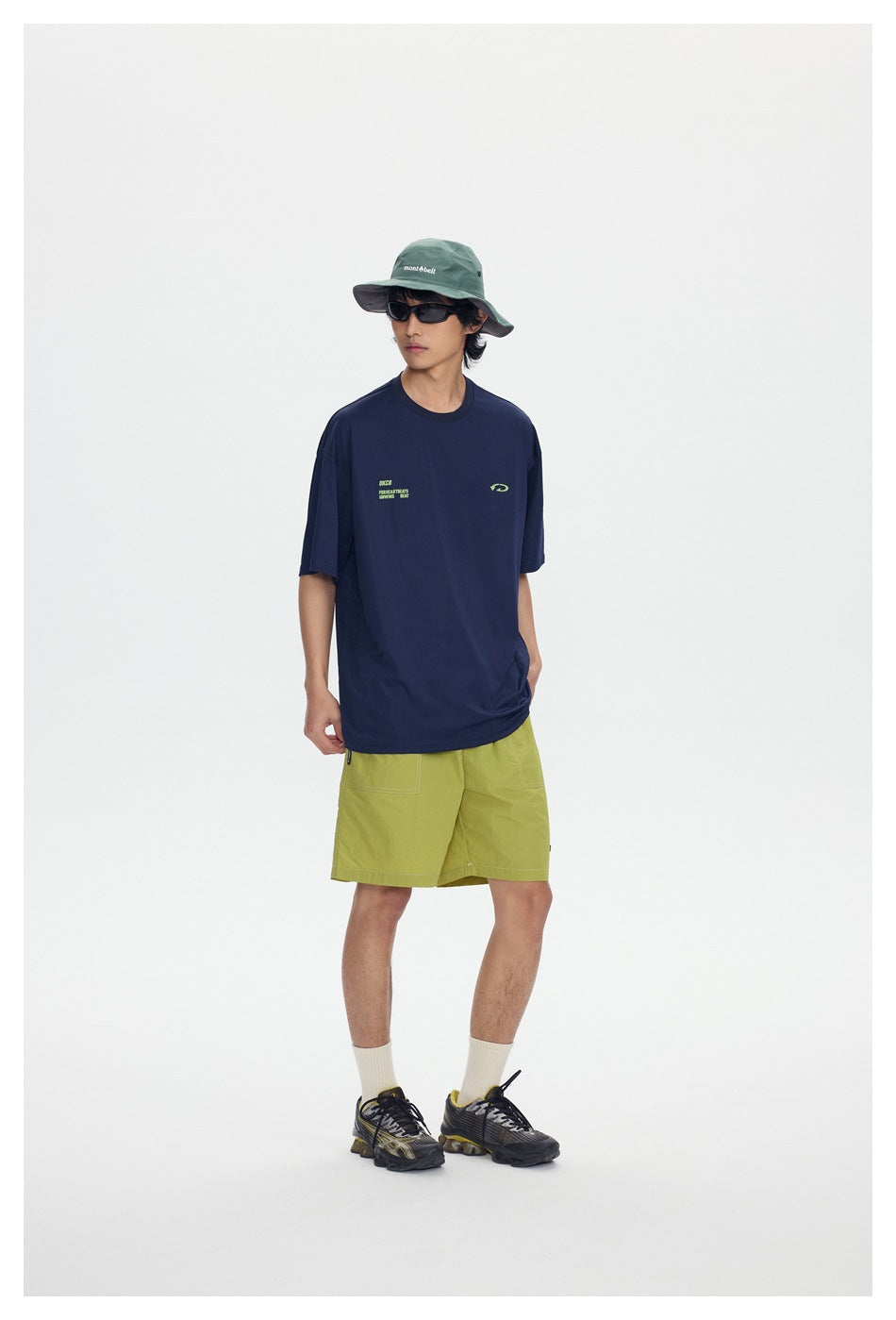Model wearing a navy short-sleeve T-shirt with small green chest print, green shorts and a bucket hat