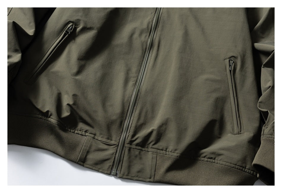 Close view of an olive green jacket front with a center zipper, two vertical zip pockets, and ribbed hem and cuffs.