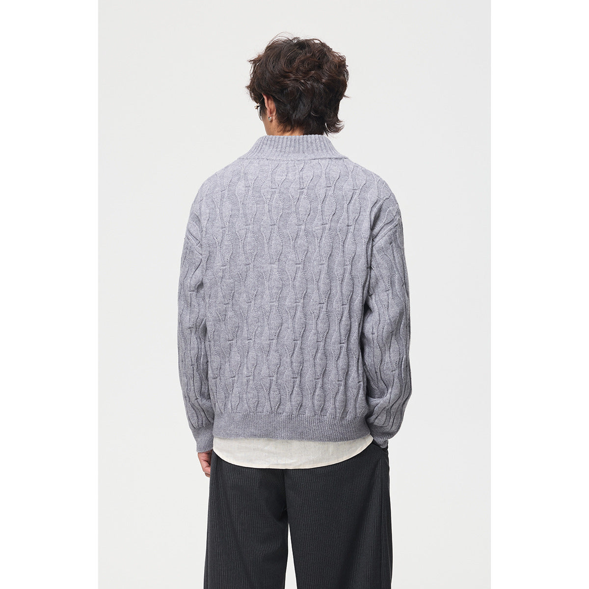 Back view of a model wearing a light gray cable-pattern sweater with a ribbed stand collar.