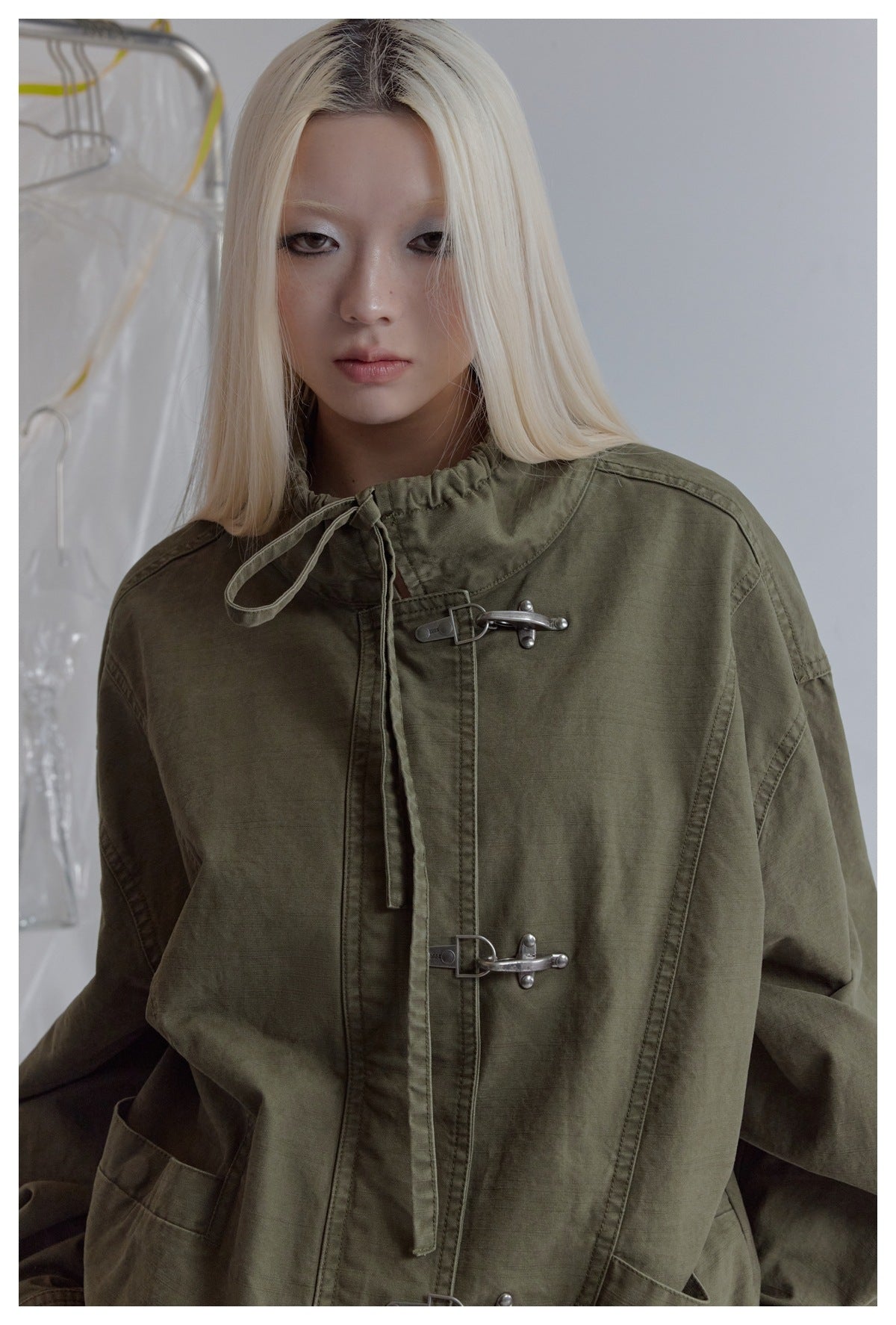 Close-up of a model wearing an olive jacket, highlighting its gathered drawstring collar and silver hook closures.