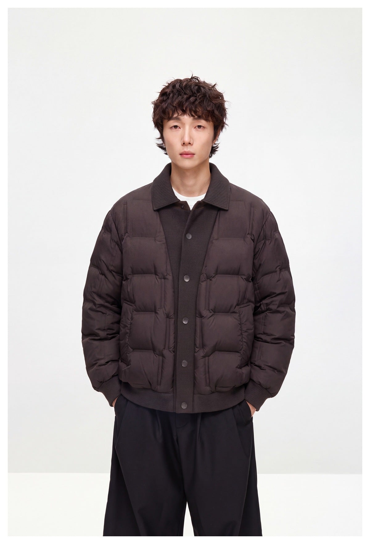 Front view of a model wearing a dark brown quilted jacket with a ribbed collar, snap front, and two patch pockets.