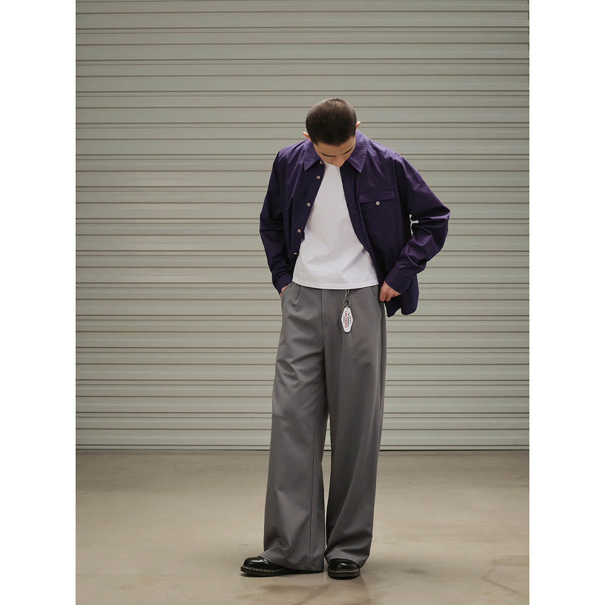 Model wearing a dark purple button-up overshirt, white T-shirt, and wide gray trousers, viewed full length.
