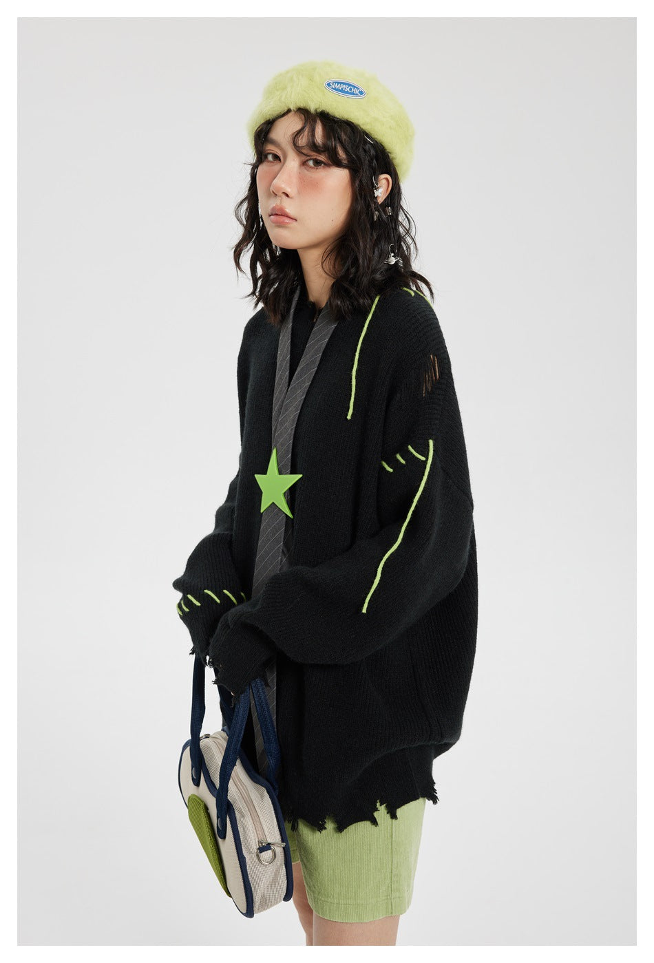 Model wearing an oversized black sweater with lime-green stitched accents and a distressed hem, shown from the front.