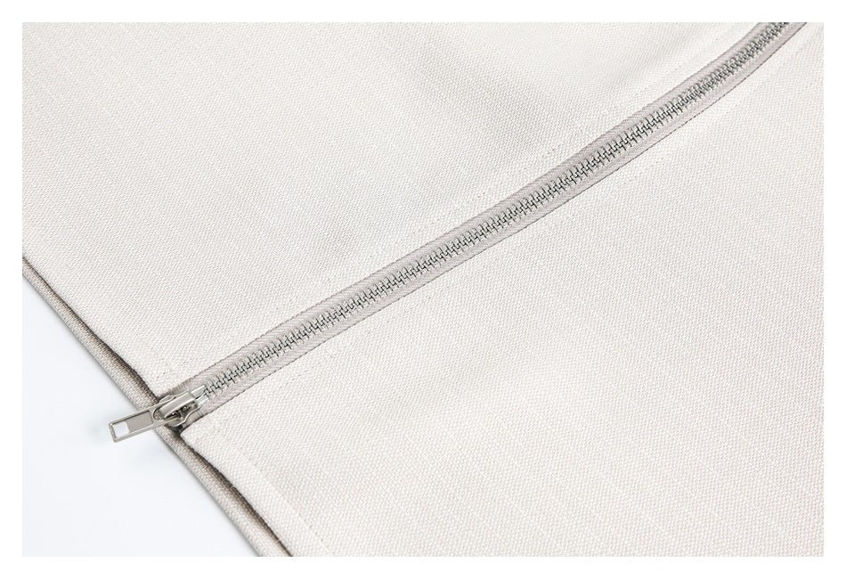 Close-up of a silver zipper running diagonally across ivory woven fabric.