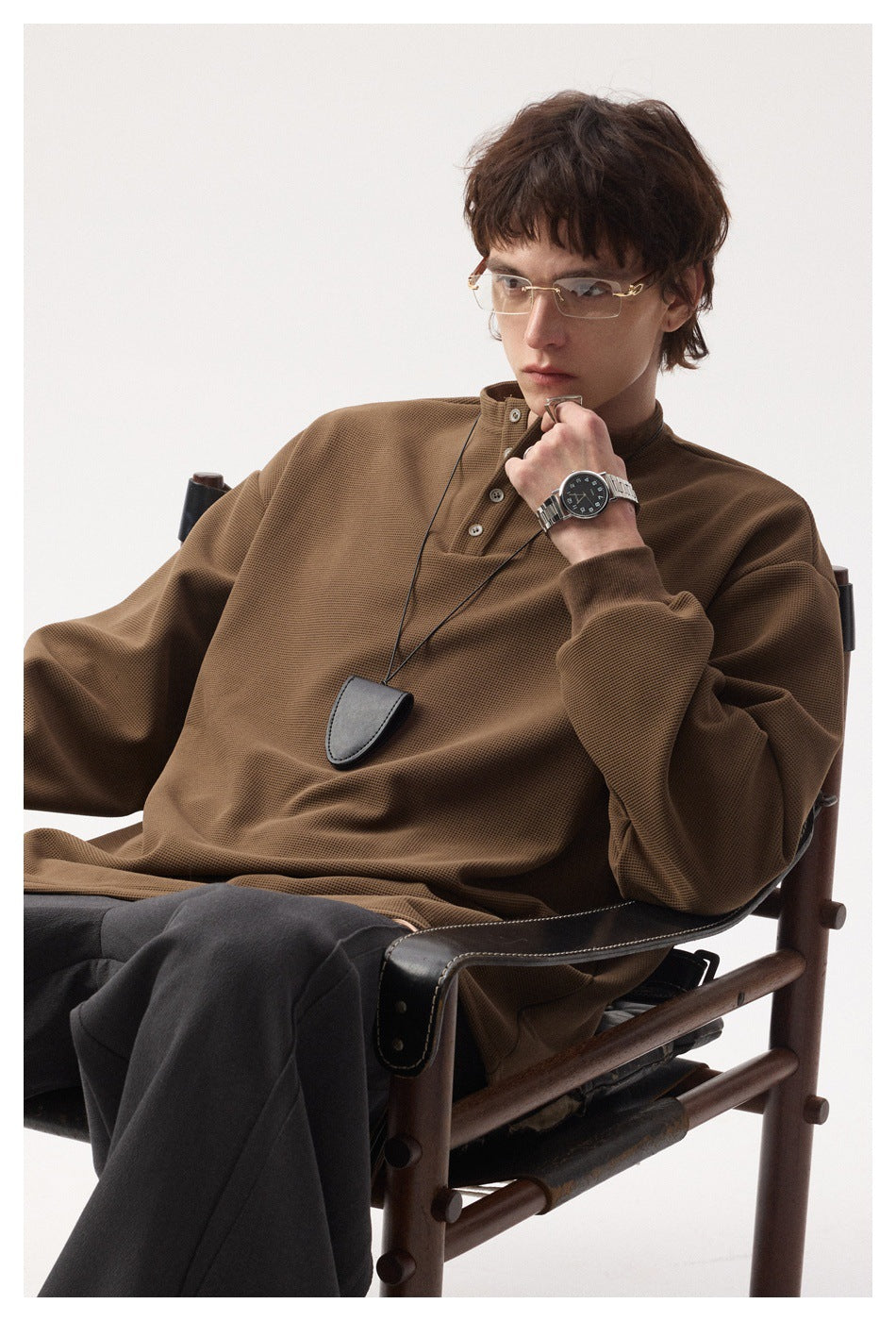 Seated model wearing a brown textured long-sleeve henley top and dark trousers.