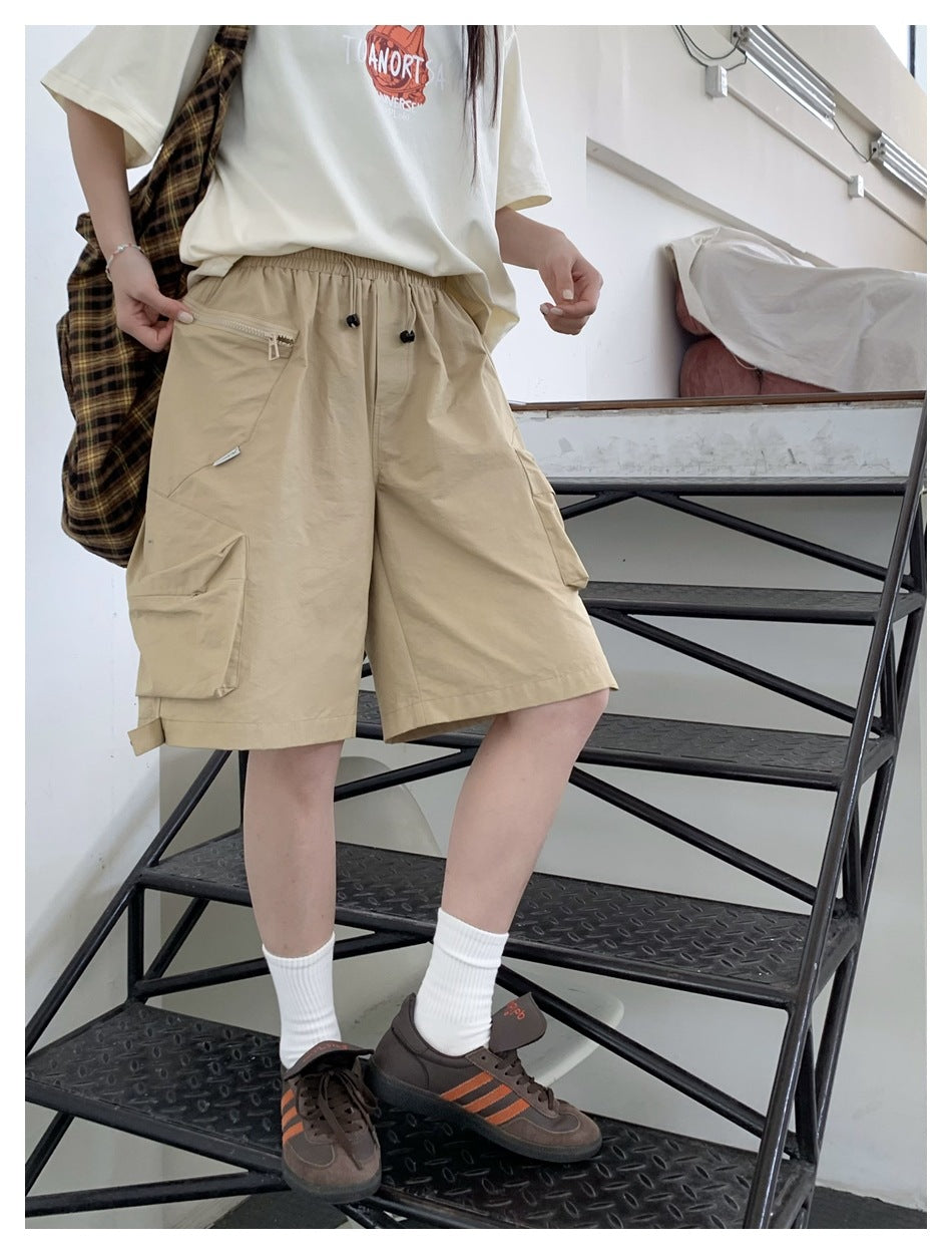 Model wearing beige cargo shorts with an elastic drawstring waist, zip pocket, and large side cargo pockets.