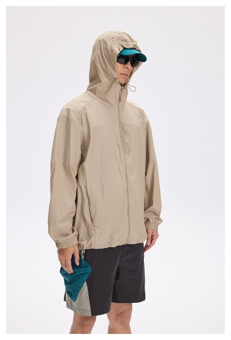 Model wearing a beige zip-front hooded jacket and dark color-block shorts, with the hood up.